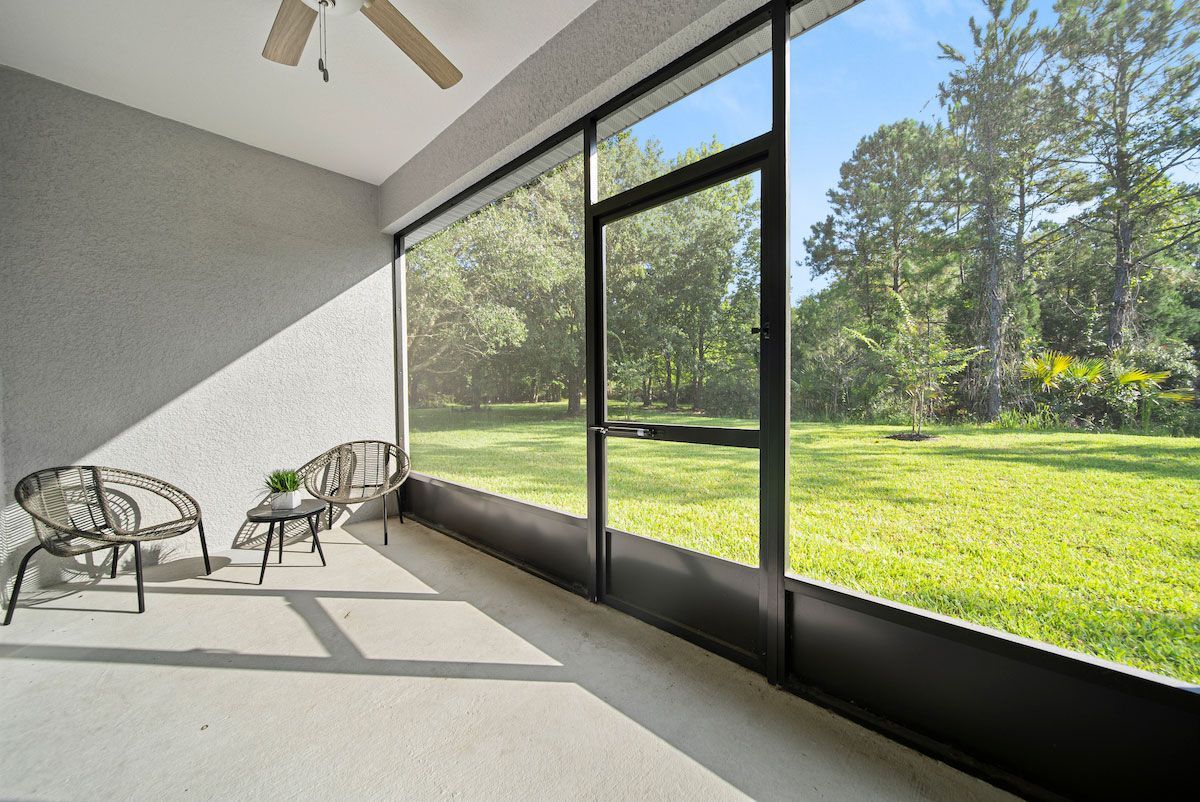A screened in porch with chairs , a table and a ceiling fan.