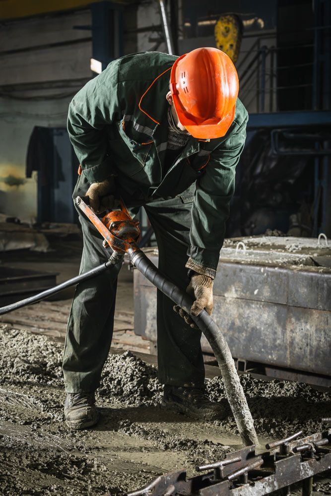 A Man Wearing A Hard Hat Is Using A Hose To Pump Concrete — JD Lynch Constructions in Cannonvale, QLD