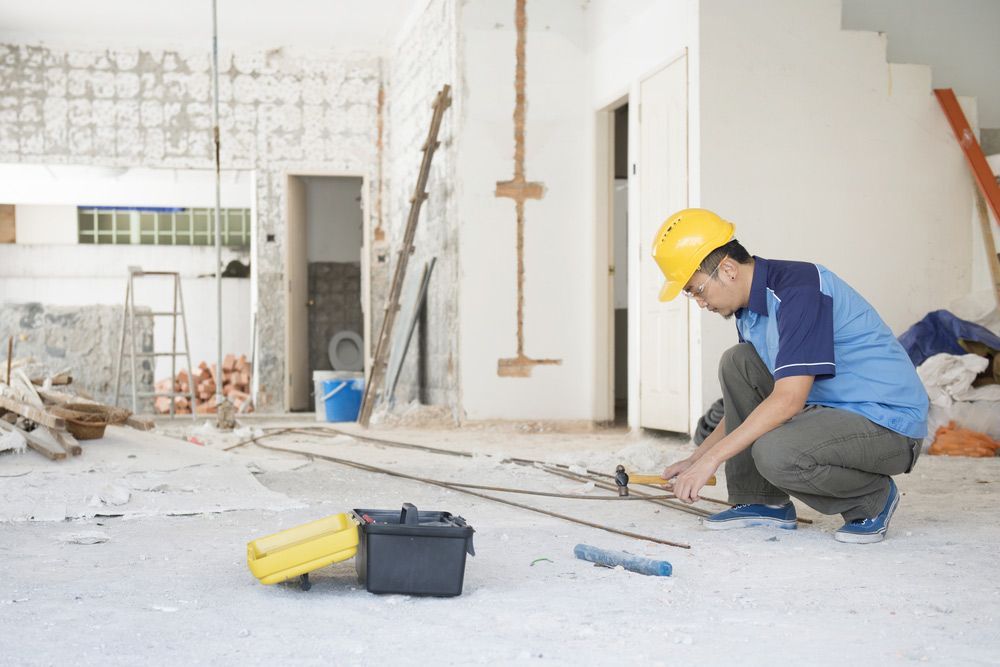 A Construction Worker Is Measuring The Floor Of A Building With A Tape Measure — JD Lynch Constructions in Cannonvale, QLD
