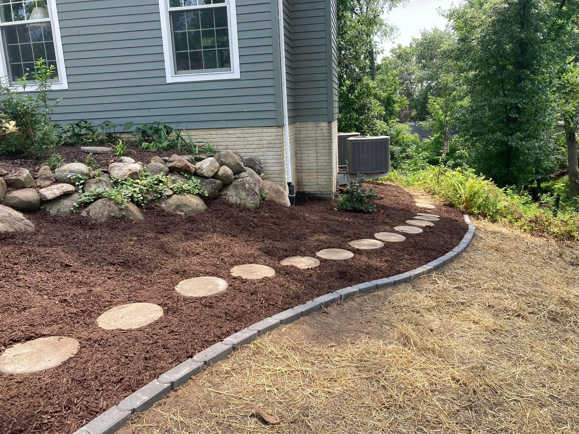 A house with landscaping, including a stepping stone path, brown mulch, and decorative rocks.