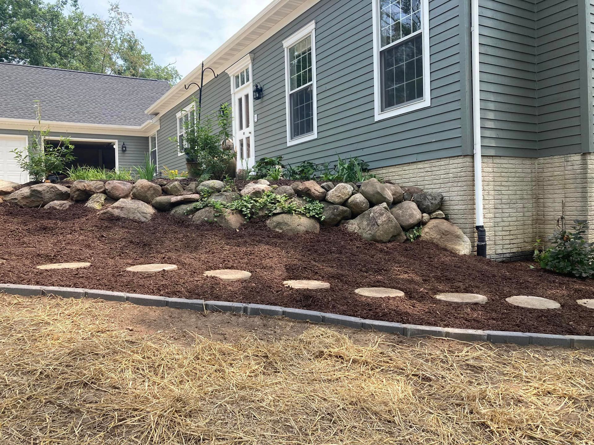 House exterior with a stone retaining wall, mulch, stepping stones, and blue-green siding.