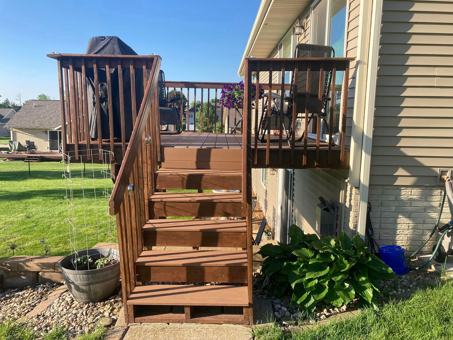 Brown wooden deck and stairs next to a beige house, overlooking a grassy yard.