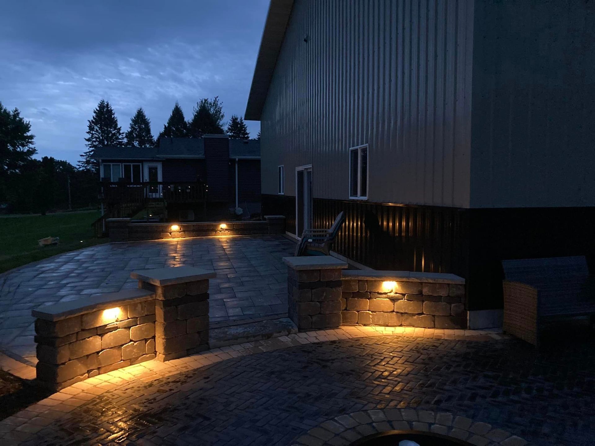 Evening patio with illuminated brick structures, pavers, and building.