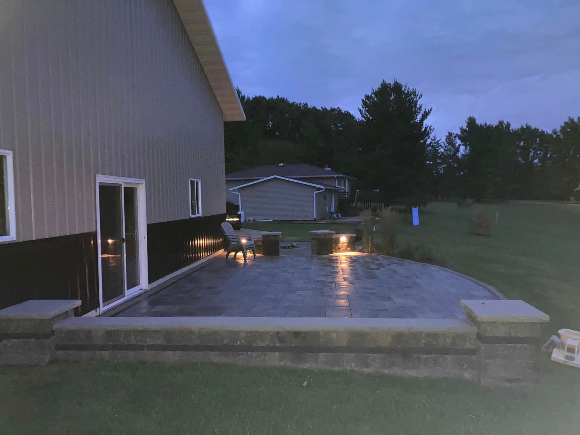 Patio at dusk with lit pavers, building, and distant houses.