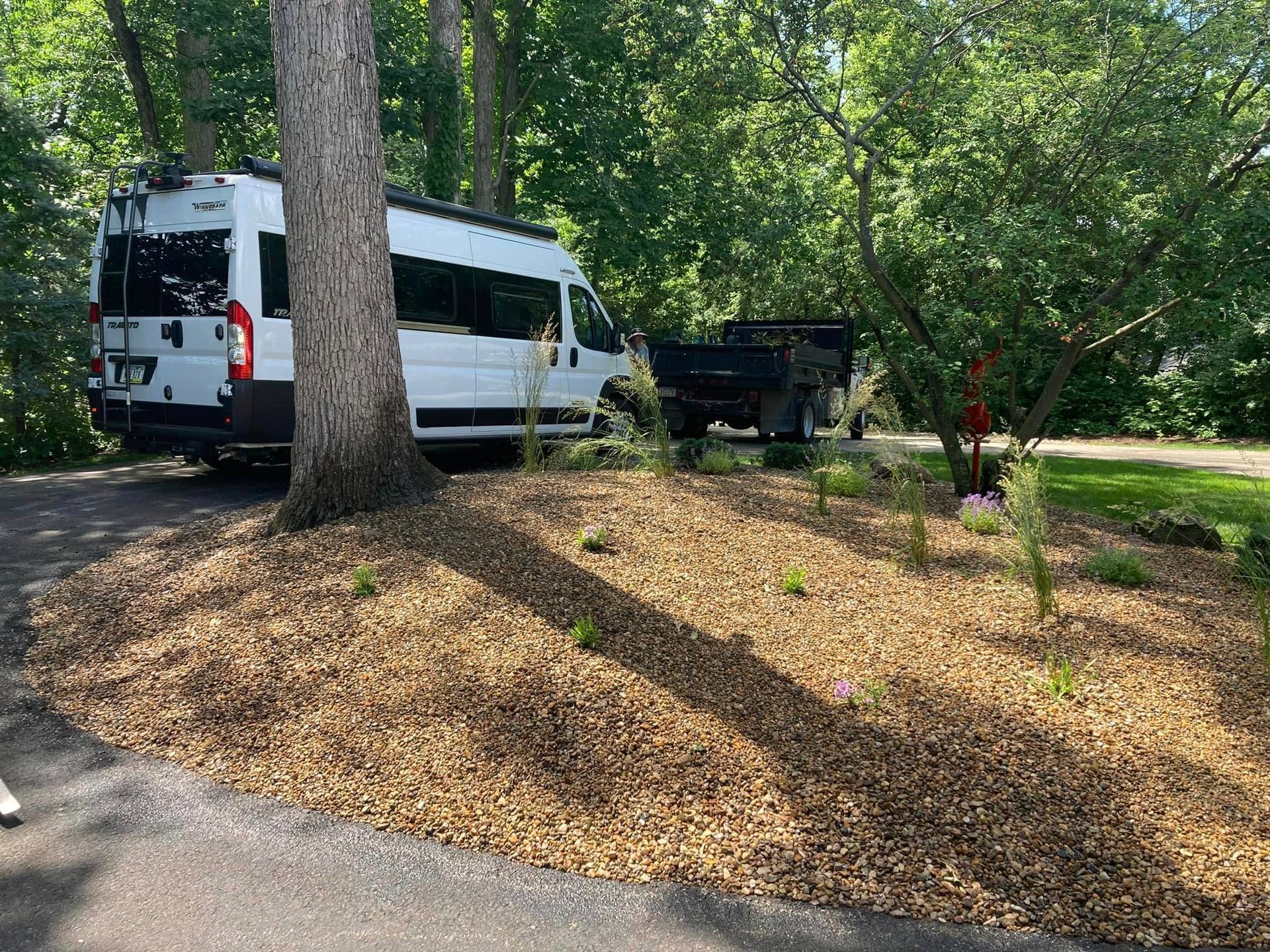 White van parked next to a tree, mulch landscaping in front, with trees in the background.