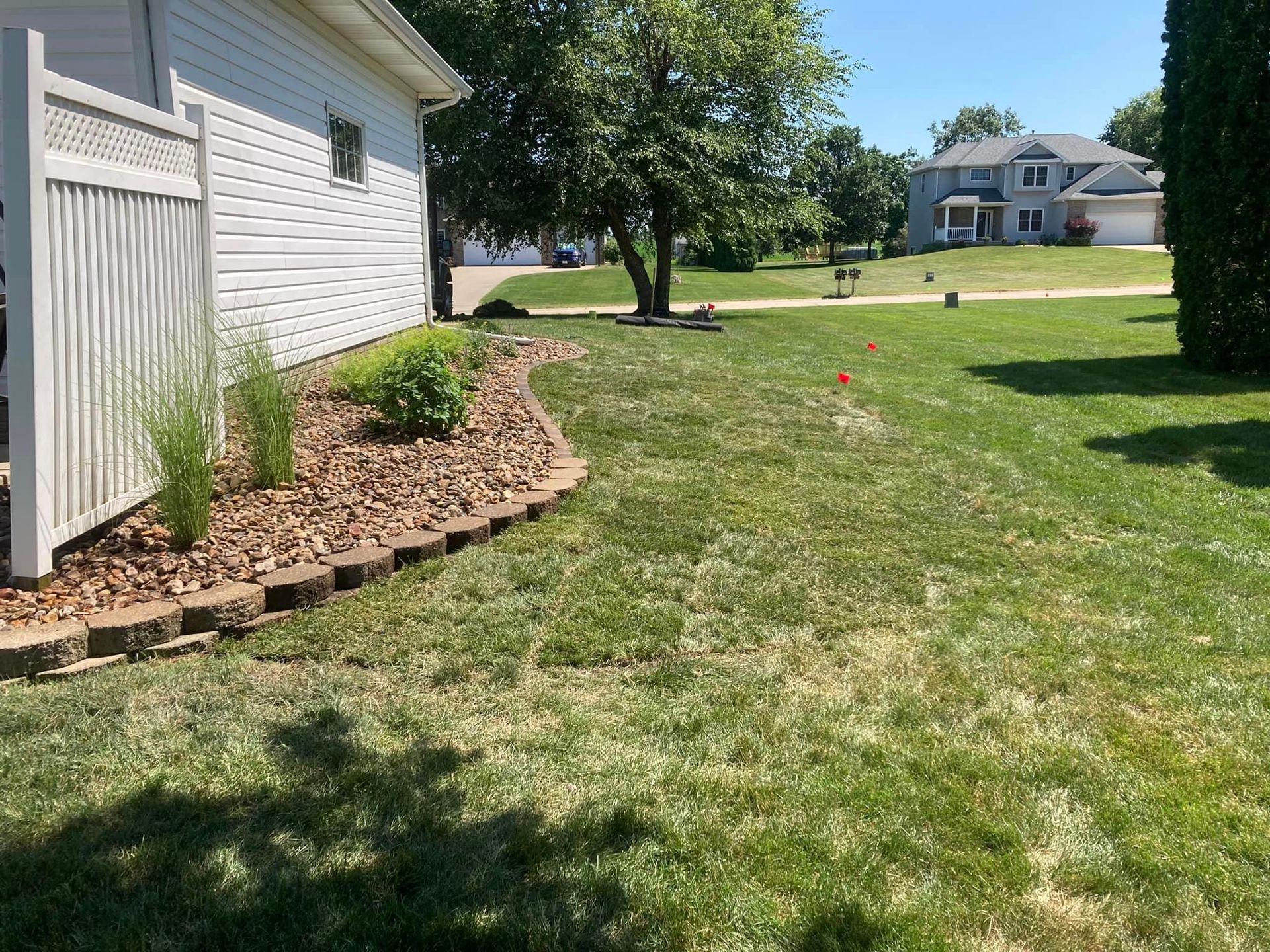 Lawn with a small garden bed and a house. Red markers in the grass, blue sky.