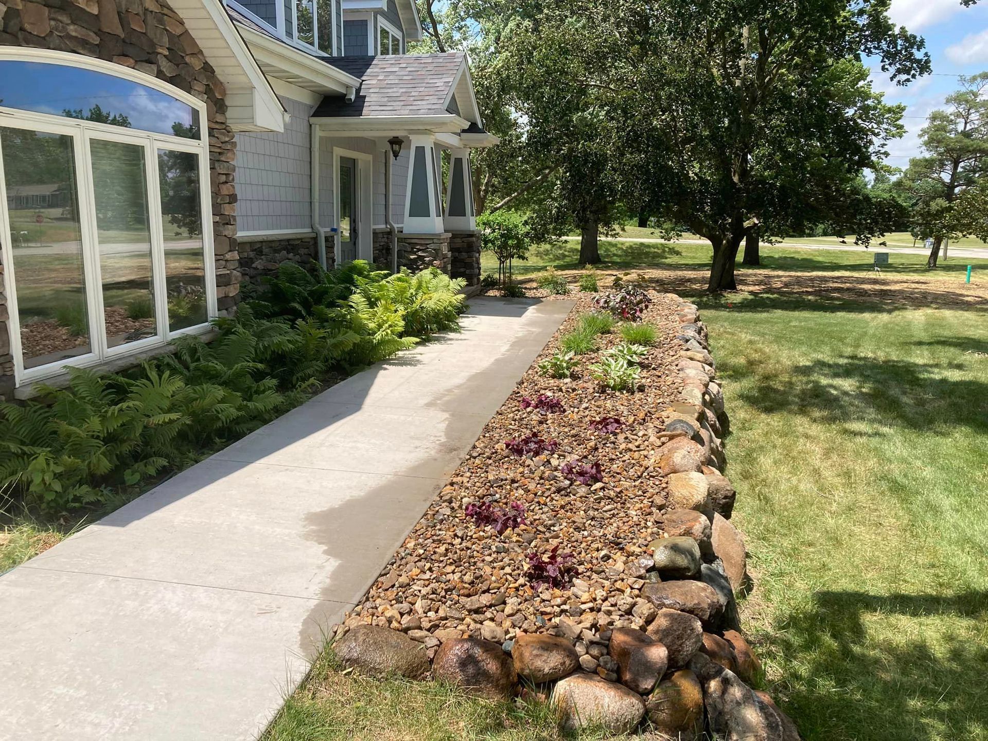 House with stone accent, concrete walkway, and rock garden with plants. Sunny day outdoors.