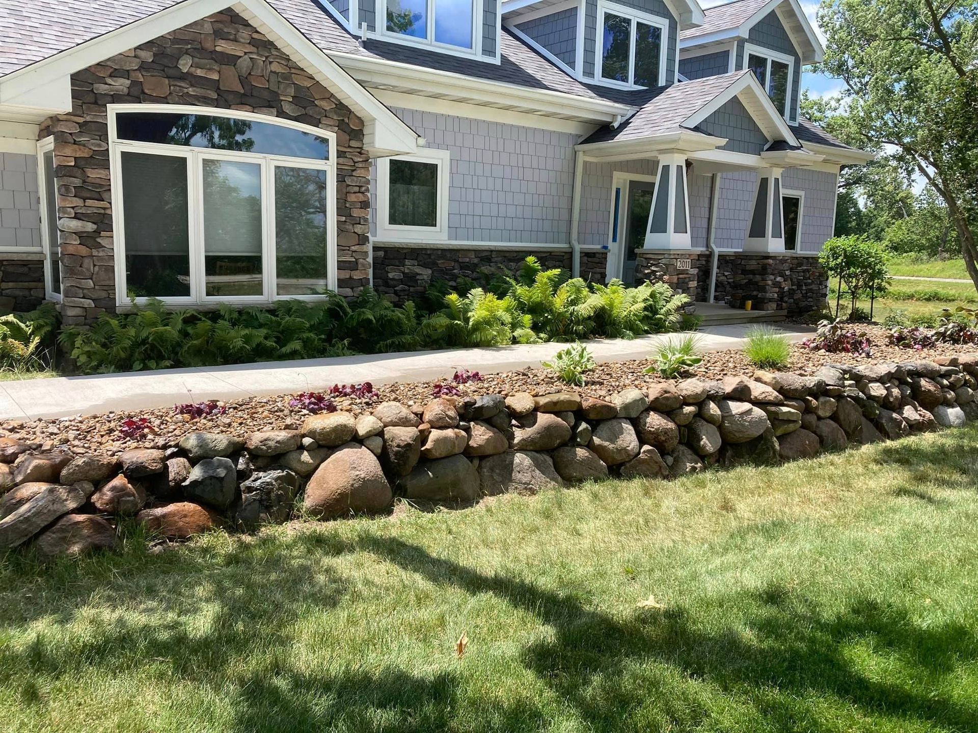 House exterior with stone and gray siding, stone retaining wall, and green lawn.