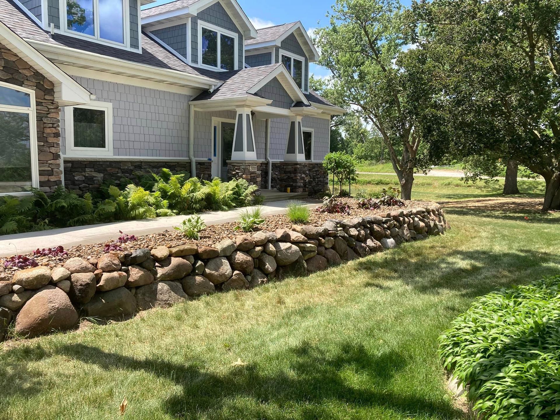 Gray house with stone wall, green lawn, and trees.