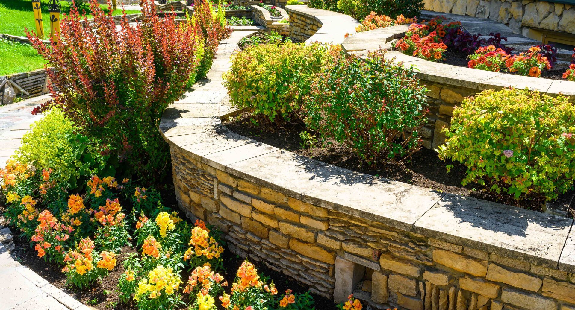 a stone wall surrounded by flowers and bushes in a garden