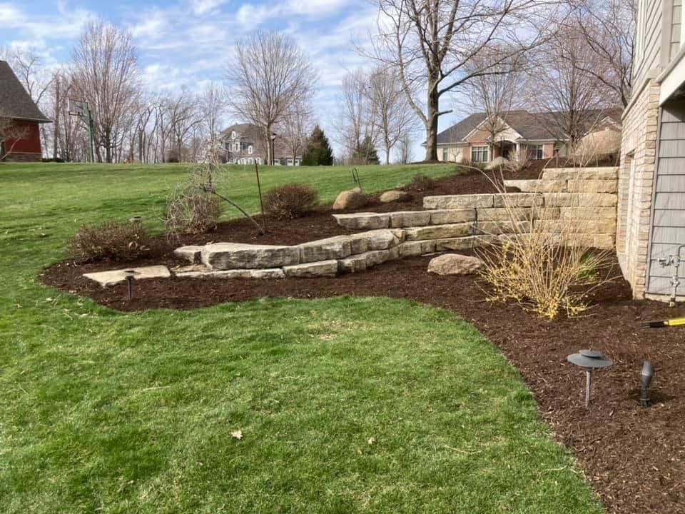 a lush green lawn with a stone wall and stairs in the backyard of a house