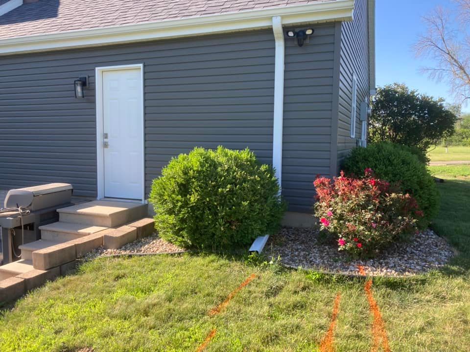 Exterior view of a building with a white door, landscaping, and a lawn under a blue sky.