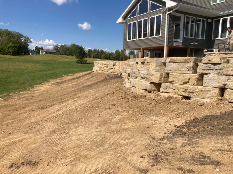 Stone retaining wall next to a house with a sloped, dirt yard.