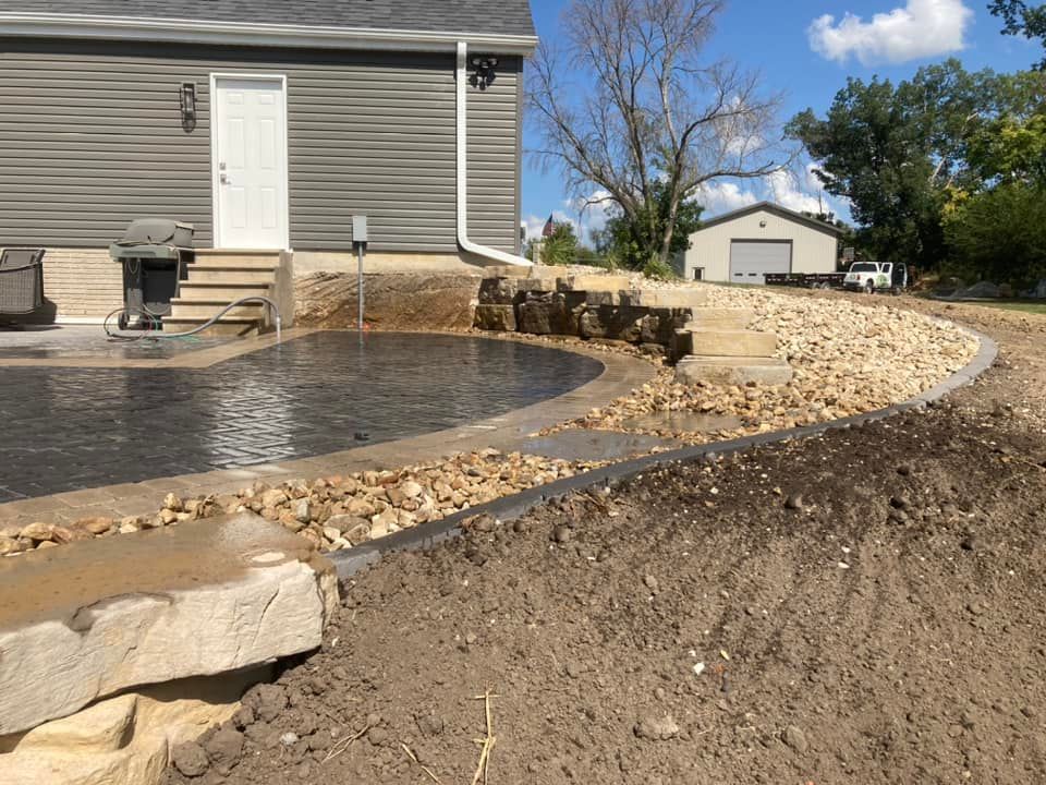Newly constructed patio area with gray house, gravel border, and a small building in the background.