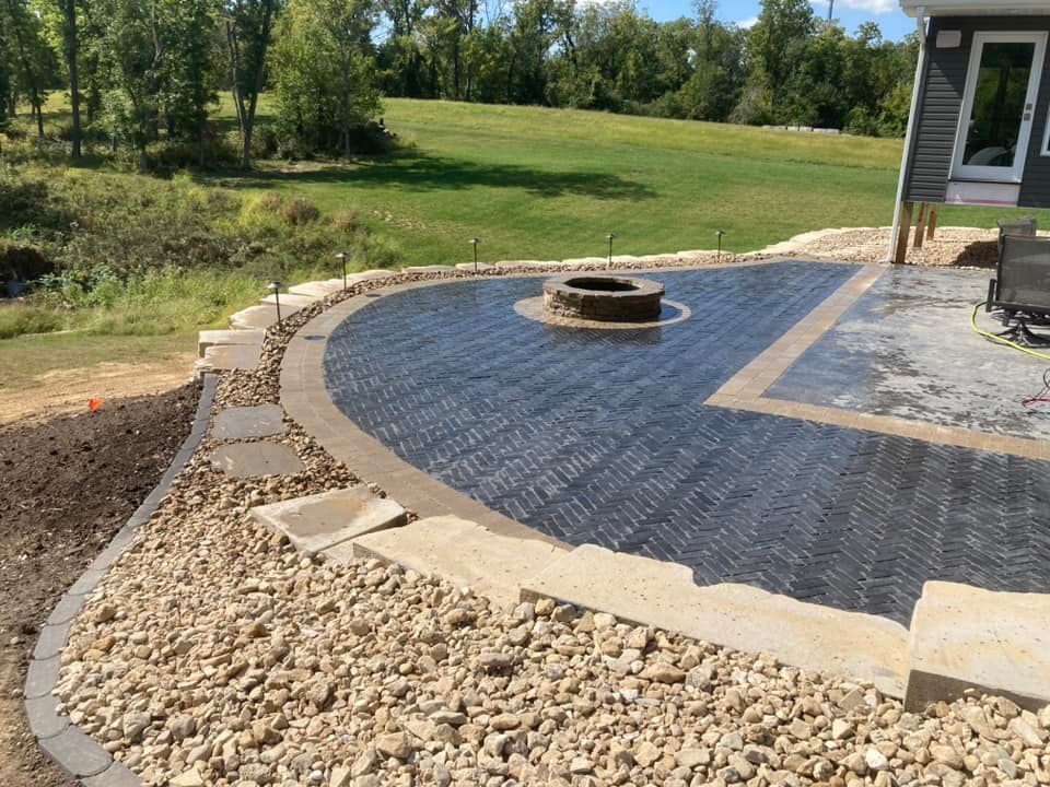 Patio with dark brickwork, fire pit, and gravel border next to a grassy lawn.