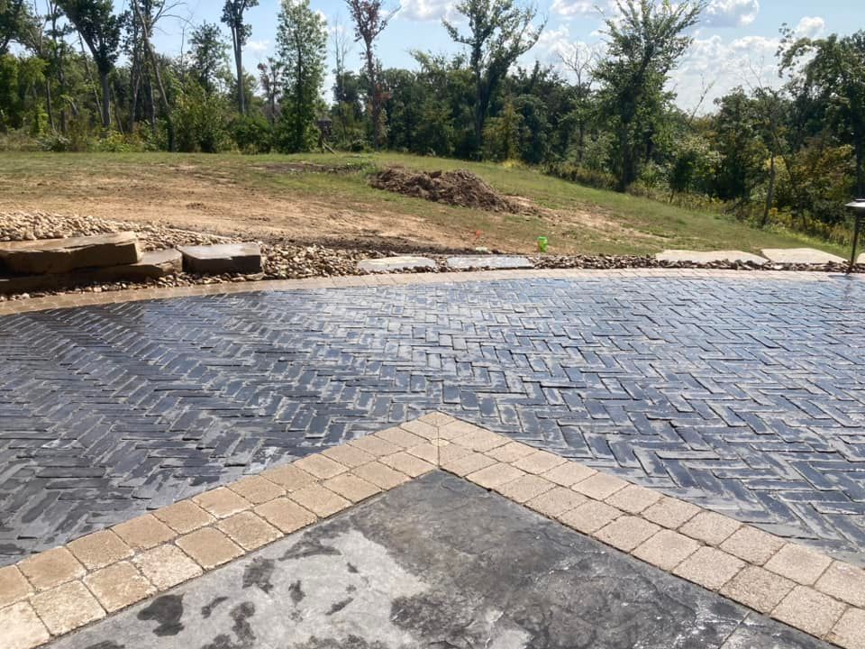 Paver patio with herringbone pattern and border, overlooking grassy hill.