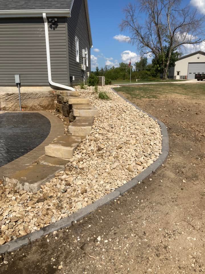 Gray-sided house with steps and gravel border along a curved driveway on a sunny day.