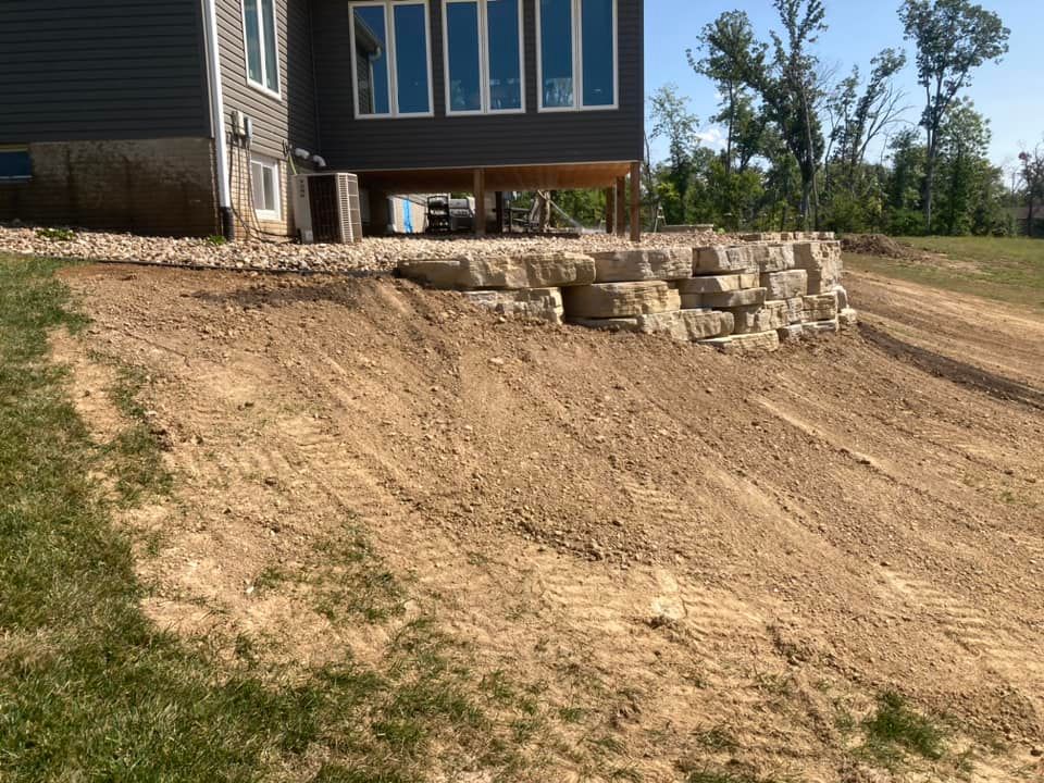 A house with a retaining wall and dirt slope in front. The sky is blue.