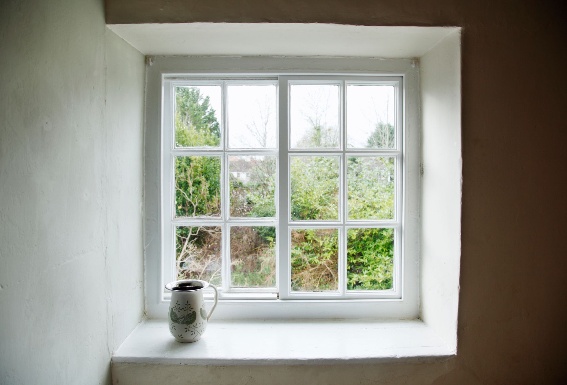 White-paned window with jug plant overlooks lush green garden. White-paned window with jug plant overlooks lush green garden.