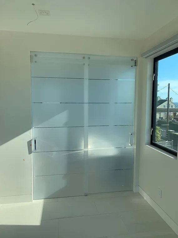 Frosted glass sliding doors with horizontal bands in a brightly lit room. A window with a view is to the right.