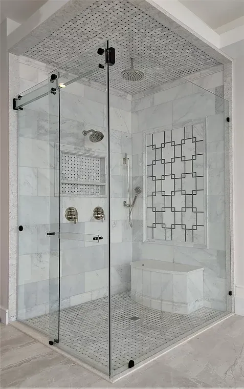 Modern shower with glass walls, white marble tile, and a decorative geometric design. Includes a showerhead.