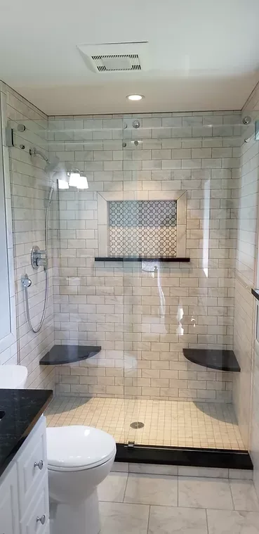 A modern bathroom with a glass-walled shower, featuring gray tile and black accents, includes a toilet and vanity.
