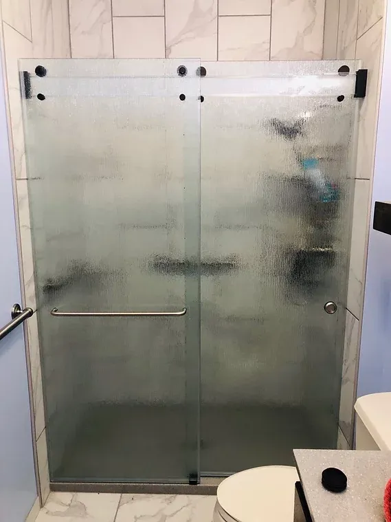 A glass shower enclosure with frosted glass doors, set against a backdrop of light blue walls and white tile.