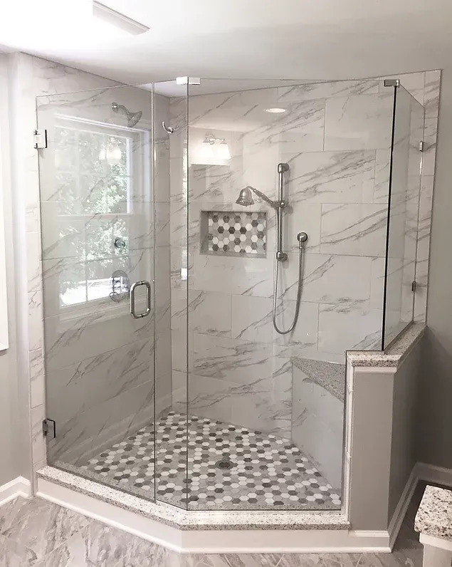 A modern corner shower with marble-look tile, glass doors, and a mosaic tile floor. It has a window, a showerhea.