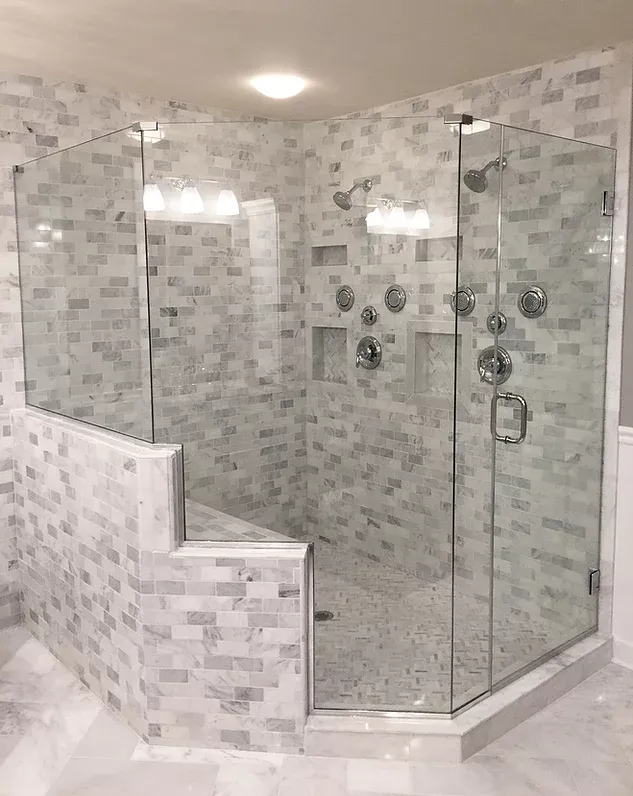 A luxurious walk-in shower with gray and white tile, a built-in bench, and glass doors. Multiple showerheads and controls.
