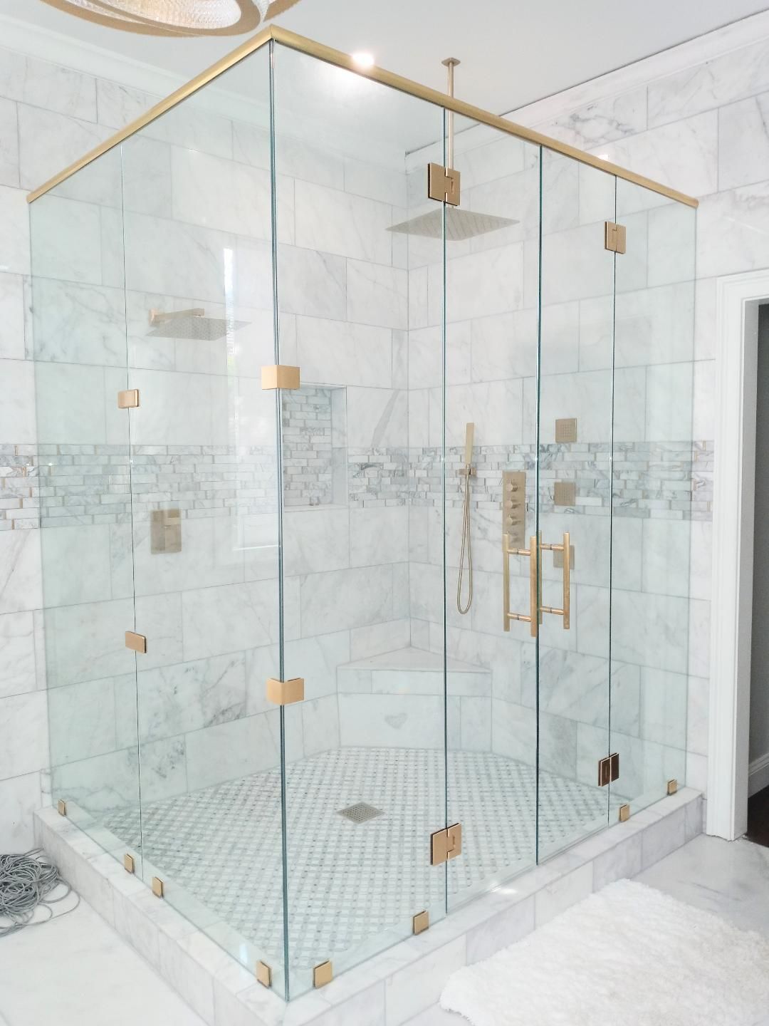 A luxurious walk-in shower with clear glass walls and gold hardware. The walls are marble, and the shower floor.