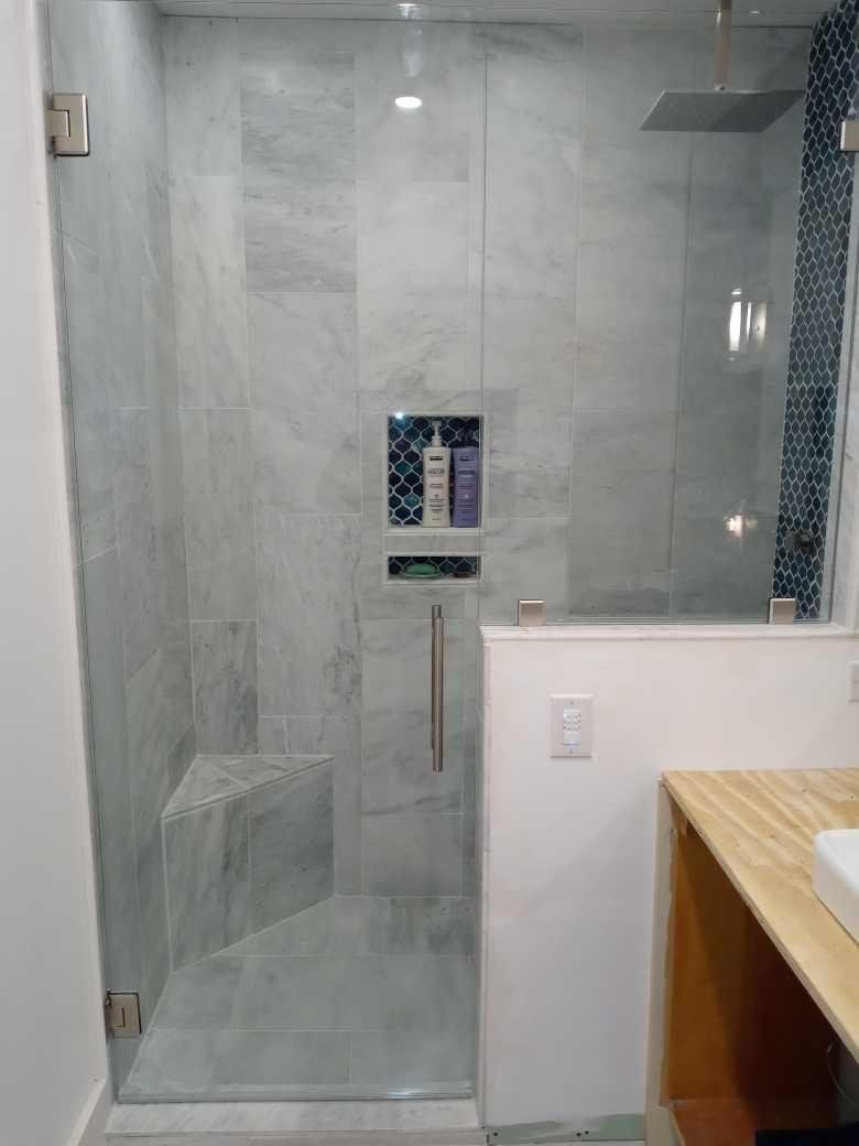 Glass-enclosed shower with gray marble-like tiles. Built-in niche with blue patterned tile holds toiletries.