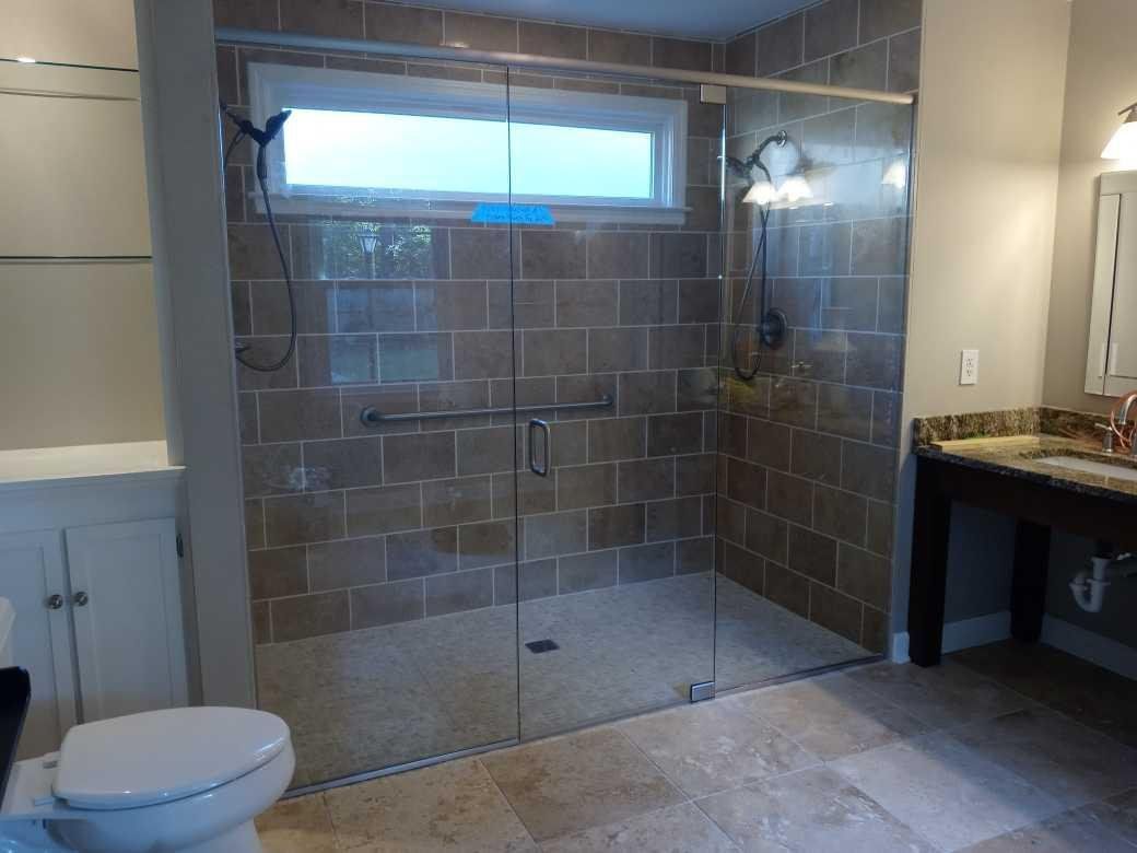 A modern bathroom with a tiled shower, glass doors, and a toilet. Beige tiles and a vanity with a brown countertop.