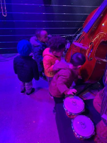 Children playing drums next to a large bass. Scene lit with blue and red lights.