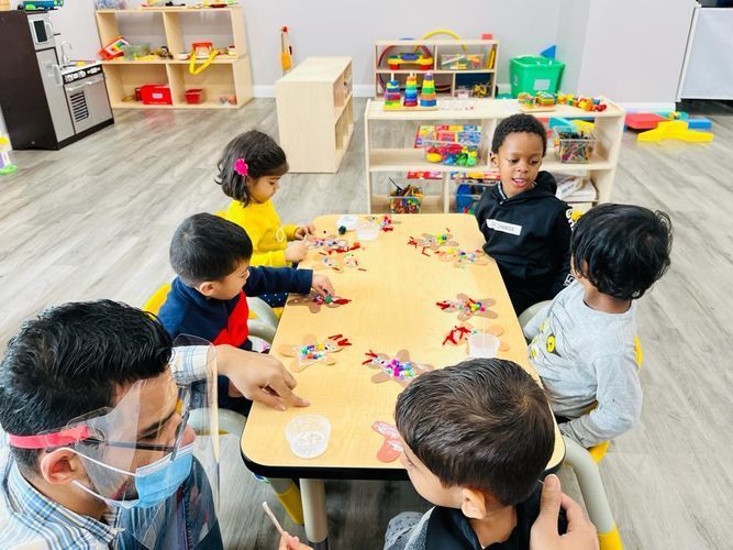 Children and teacher at a table, working on puzzle. Classroom setting, multi-ethnic kids smiling.