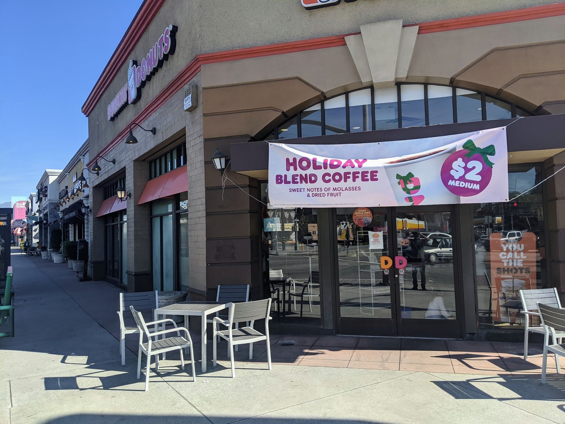 Exterior view of a Dunkin' store with outdoor seating and a Holiday Blend coffee promotional banner over the entrance.