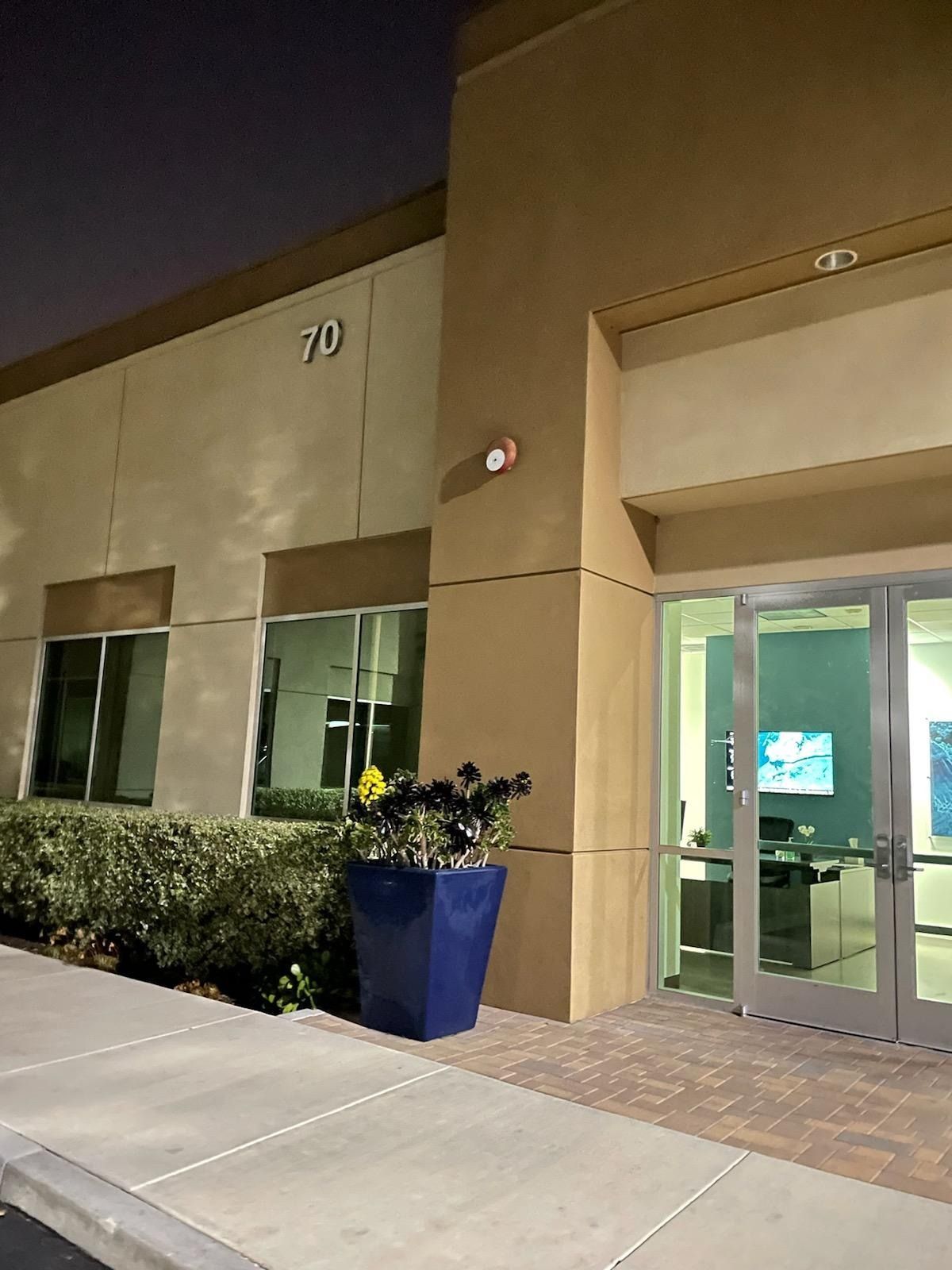 Entrance to a commercial building with a blue planter by the glass doors and the number 70 on the beige exterior wall.