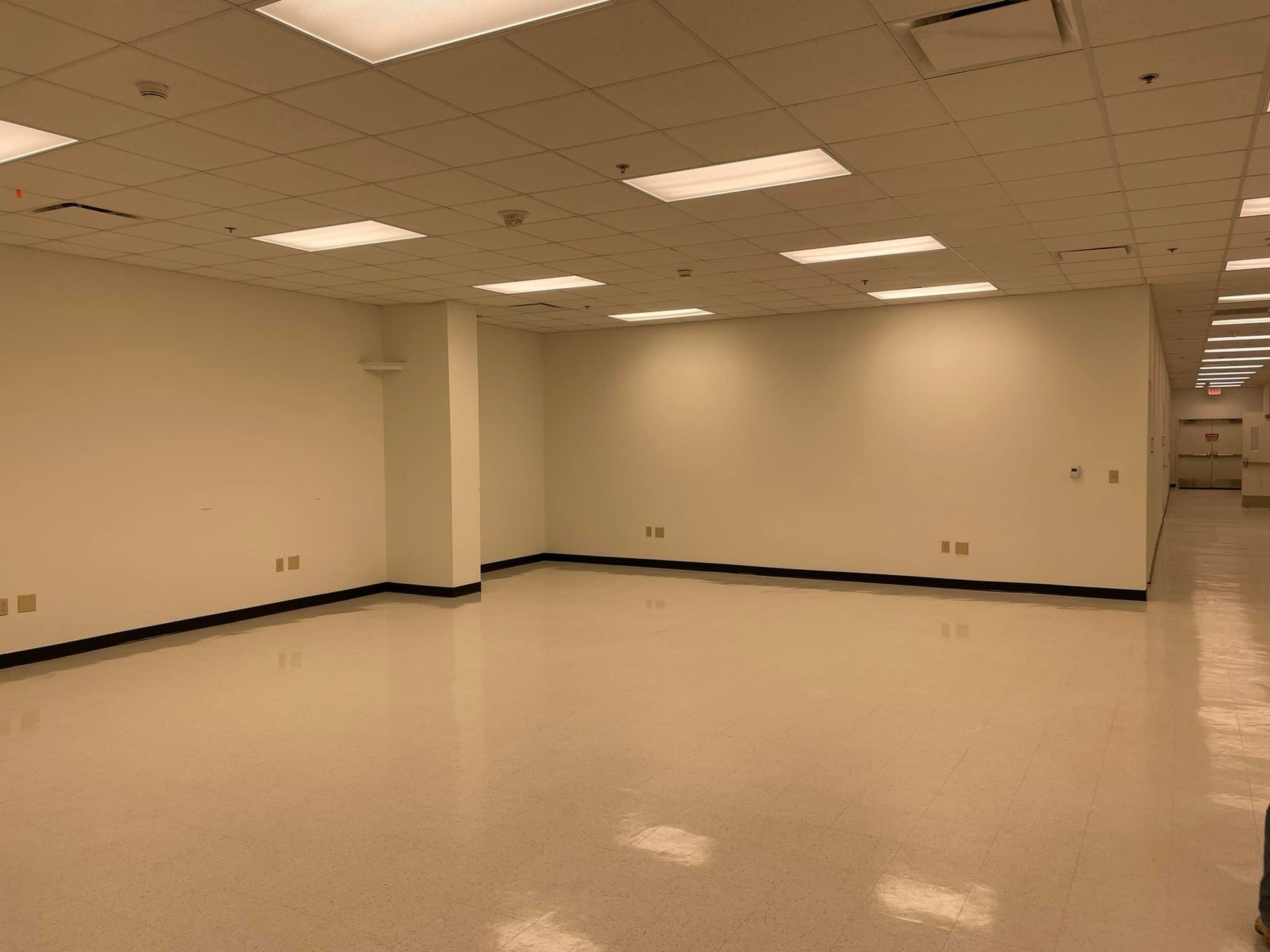 An empty, brightly lit office or commercial space with off-white walls, a tiled ceiling, and a polished floor.