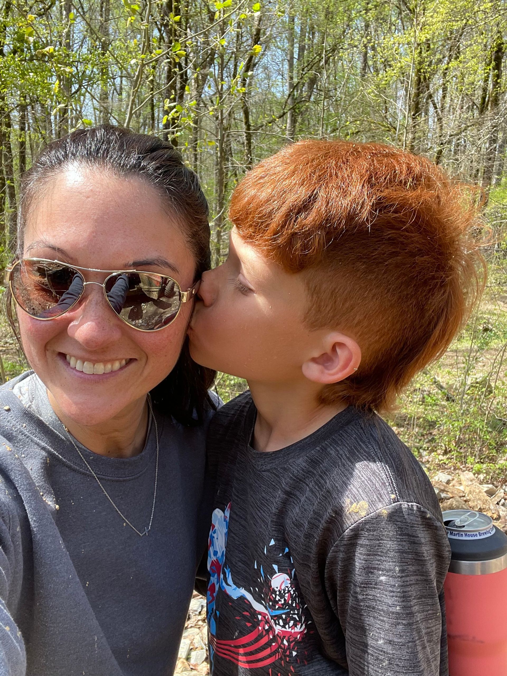 A boy is kissing a woman on the cheek while wearing sunglasses.