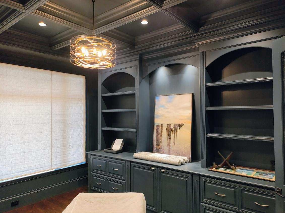 Dark-paneled study with built-in bookshelves, an arched alcove with art, and a decorative light fixture.