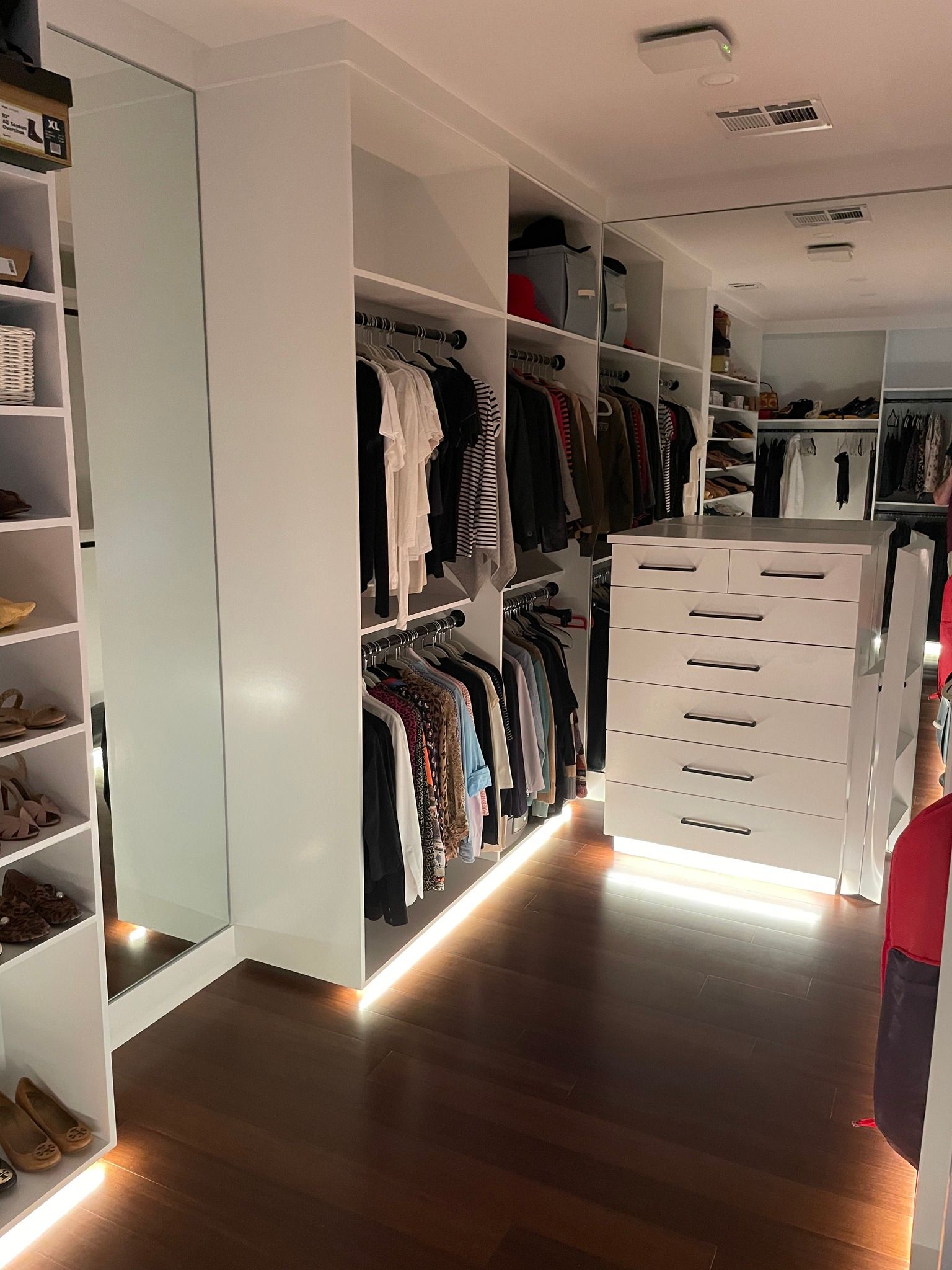 White closet with clothes hanging. Shelves for shoes. Dark wood floor.
