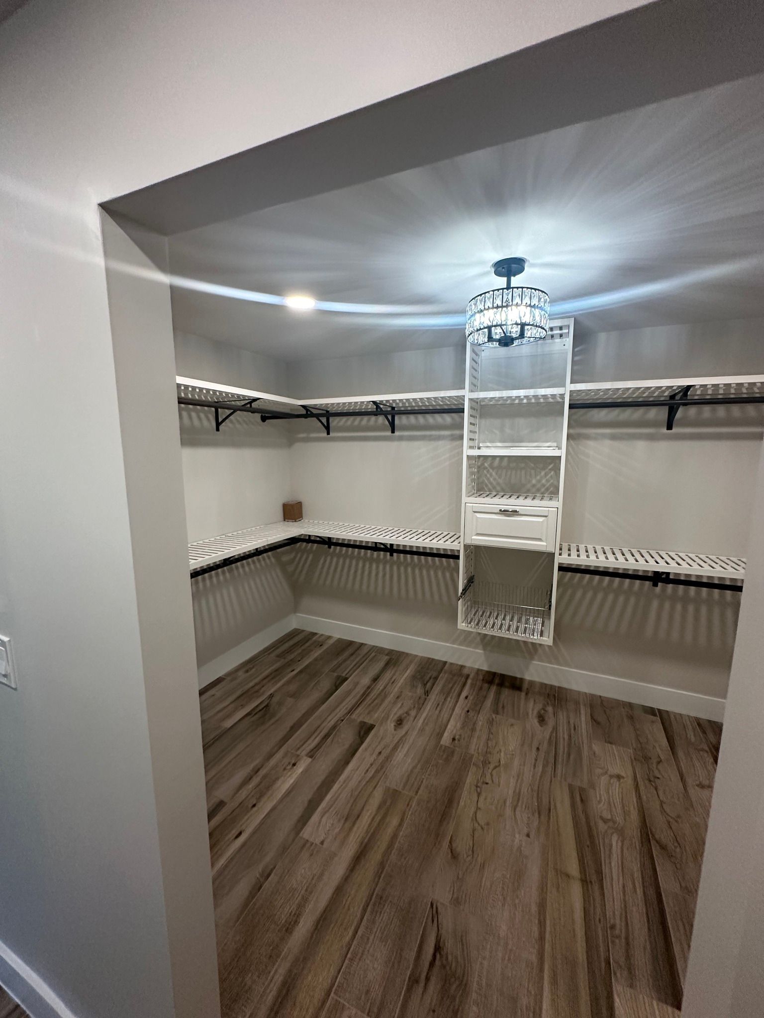 Empty walk-in closet with shelves and drawers.  Wooden floor, white walls. Bright overhead light.