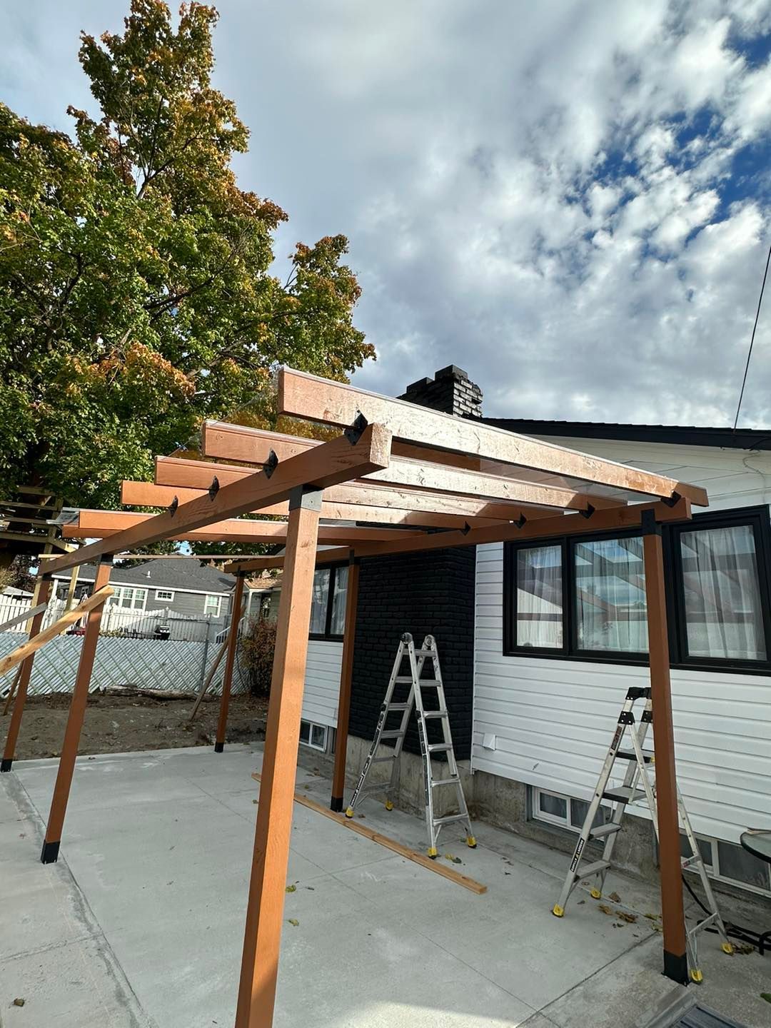 Wooden pergola attached to a white house, with a ladder and tools present.