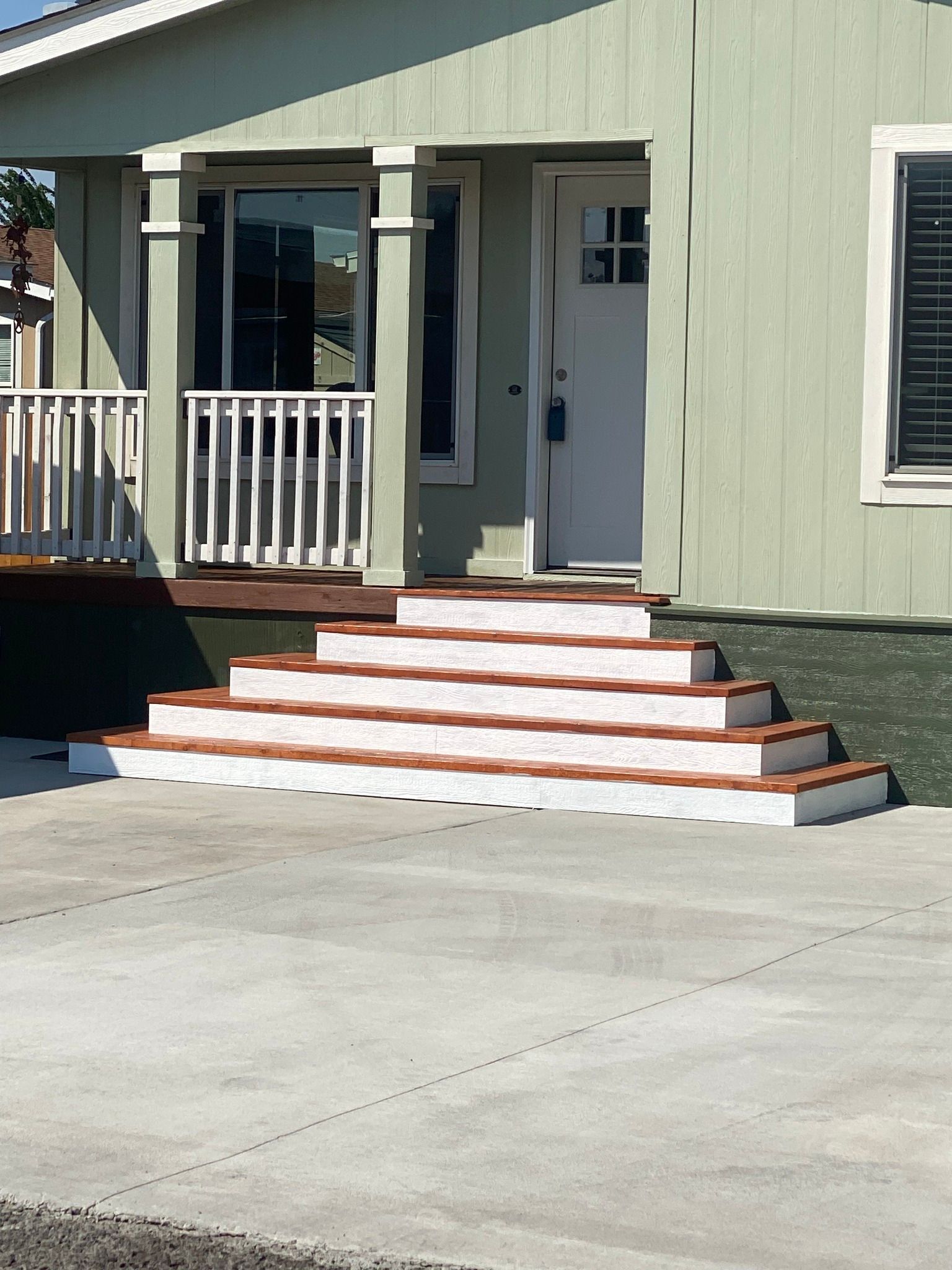 Light green house with steps leading up to a white door. Concrete driveway in front.