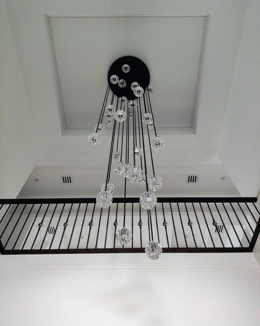 Ornate chandelier hanging from a white ceiling, above a black railing.