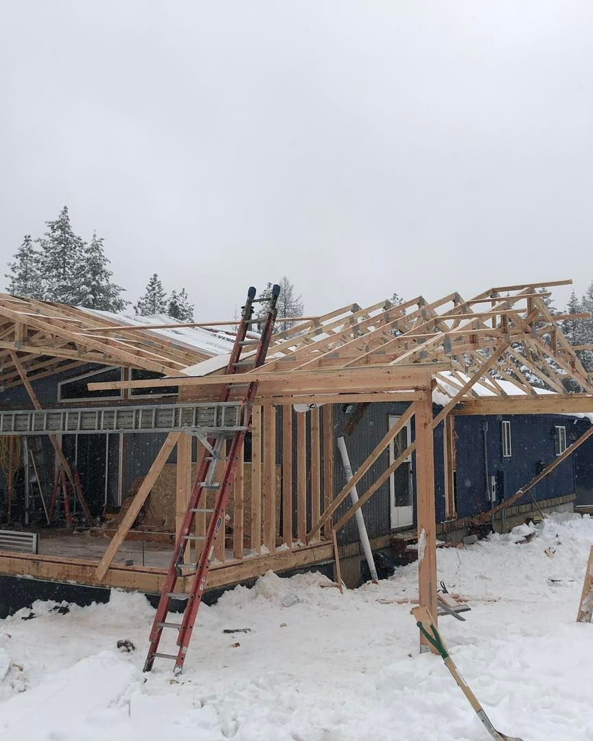 Construction site in winter, framing a house with snow on the ground, ladders leaning against the structure.