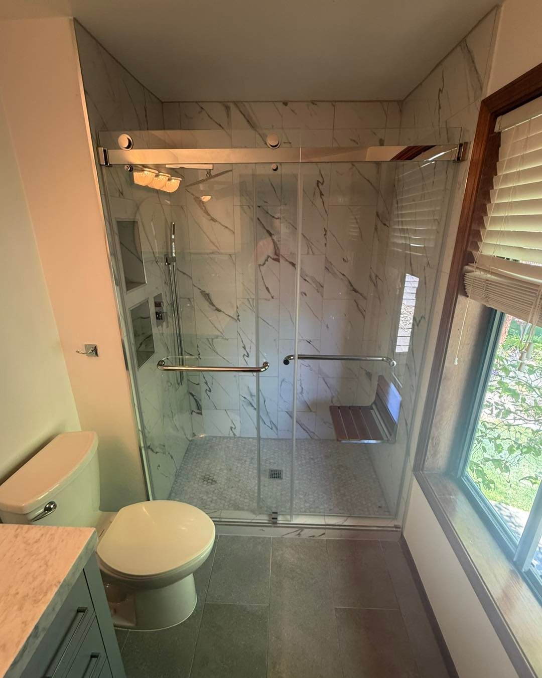 Bathroom with a tiled shower, toilet, and a window with a blind.