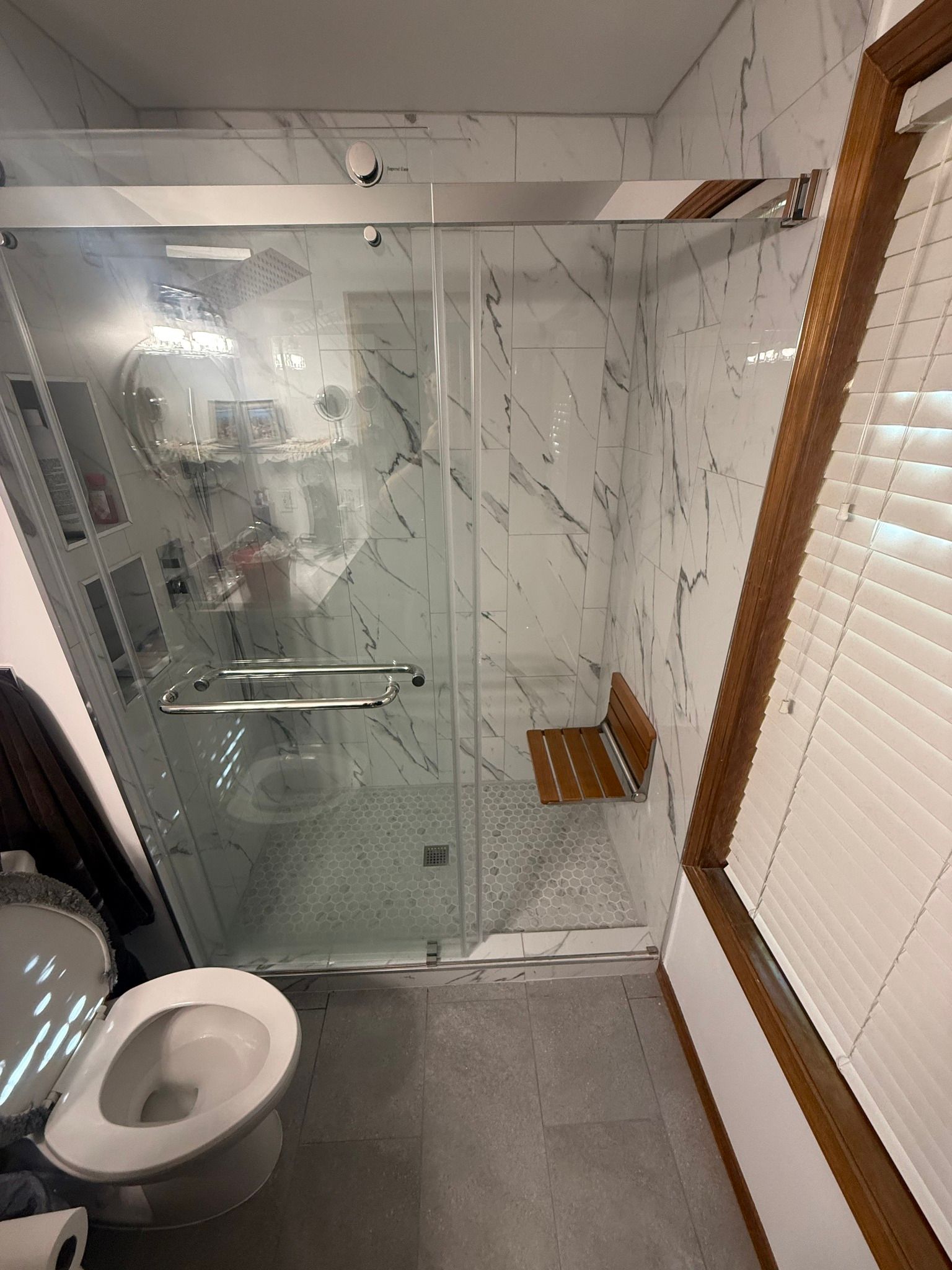 Bathroom with a glass shower, toilet, and marble tile walls.