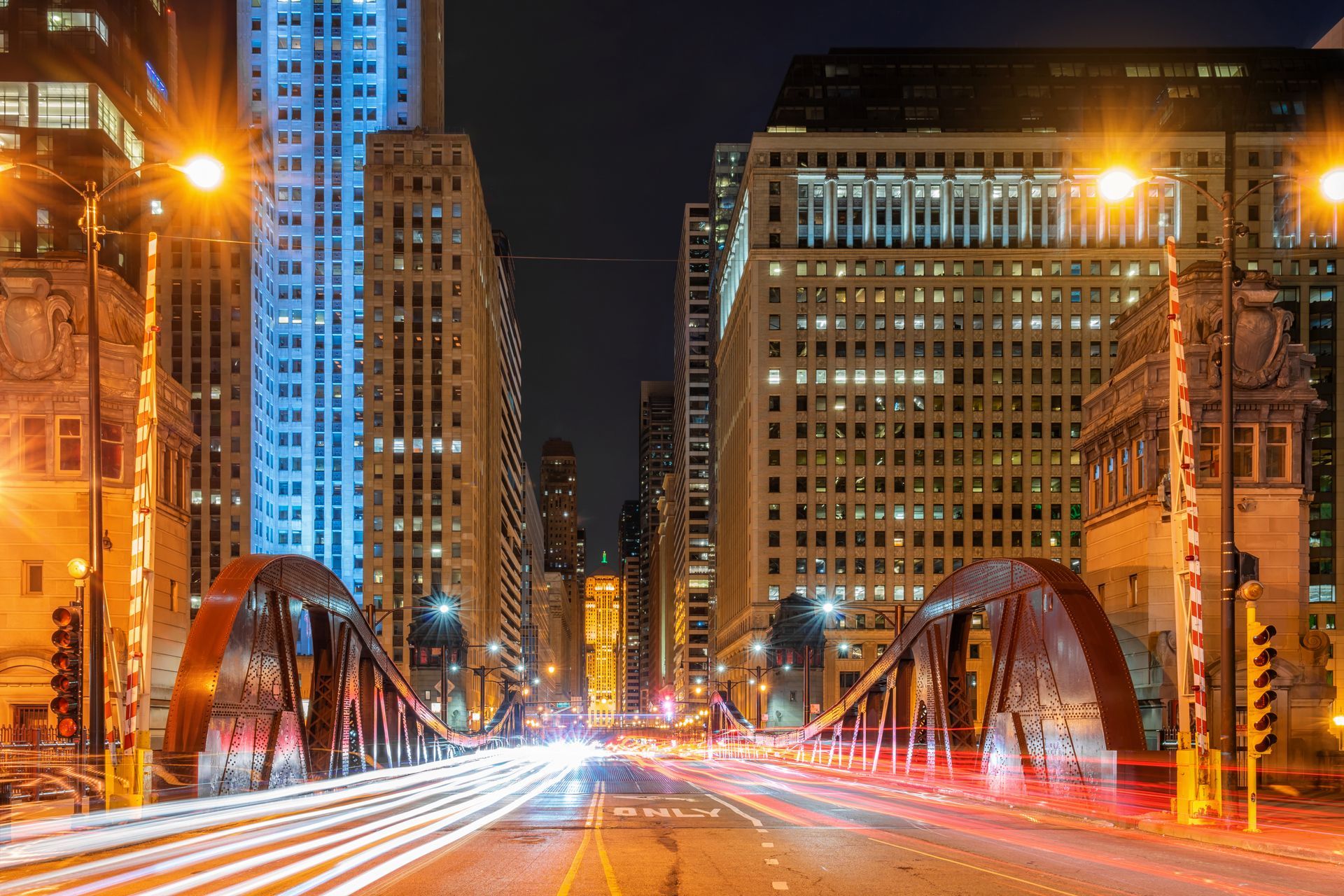 A city street at night with a bridge in the foreground and buildings in the background.