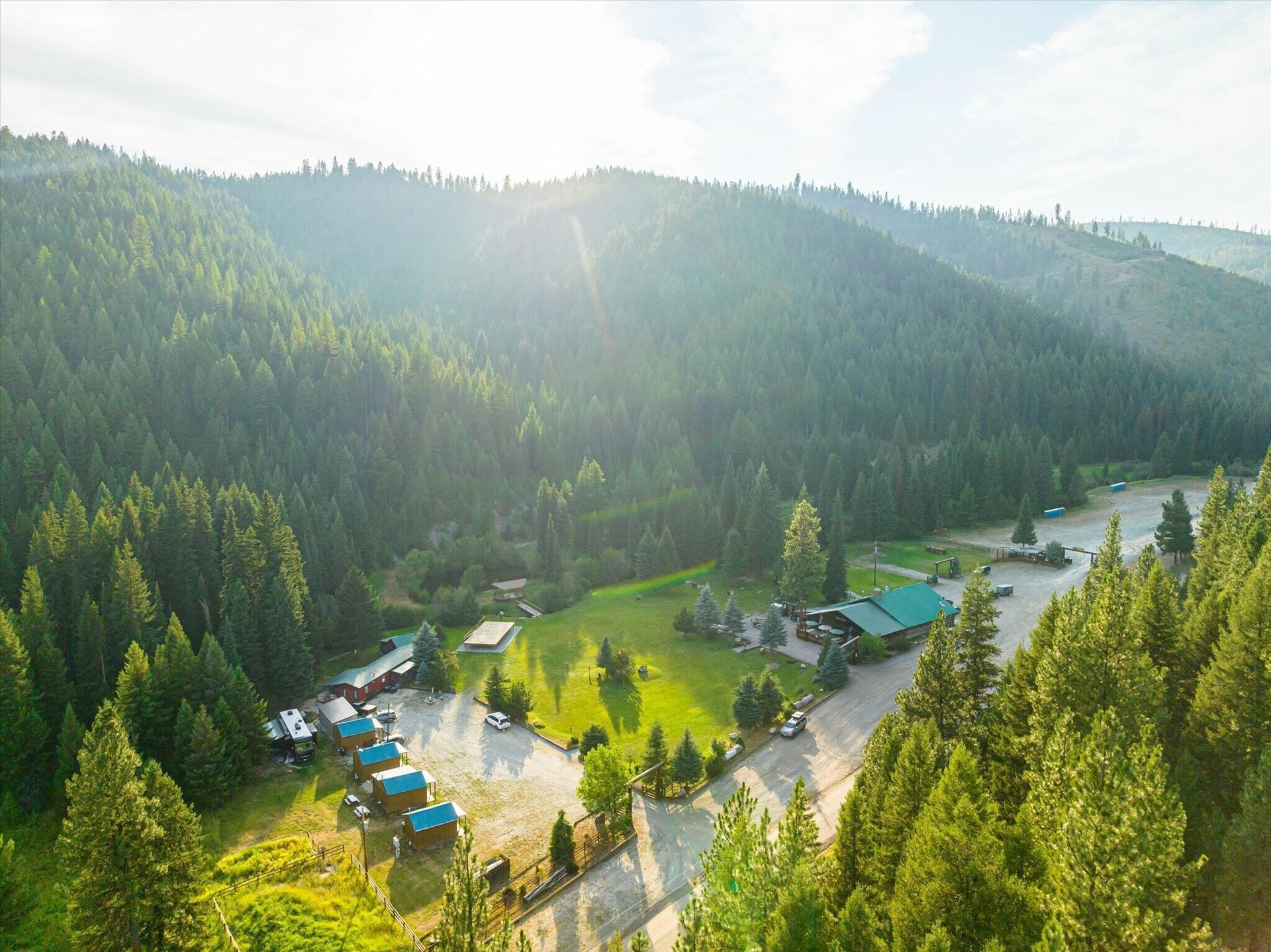 Aerial view of a forested valley with cabins, a road, and a river in bright morning sunlight