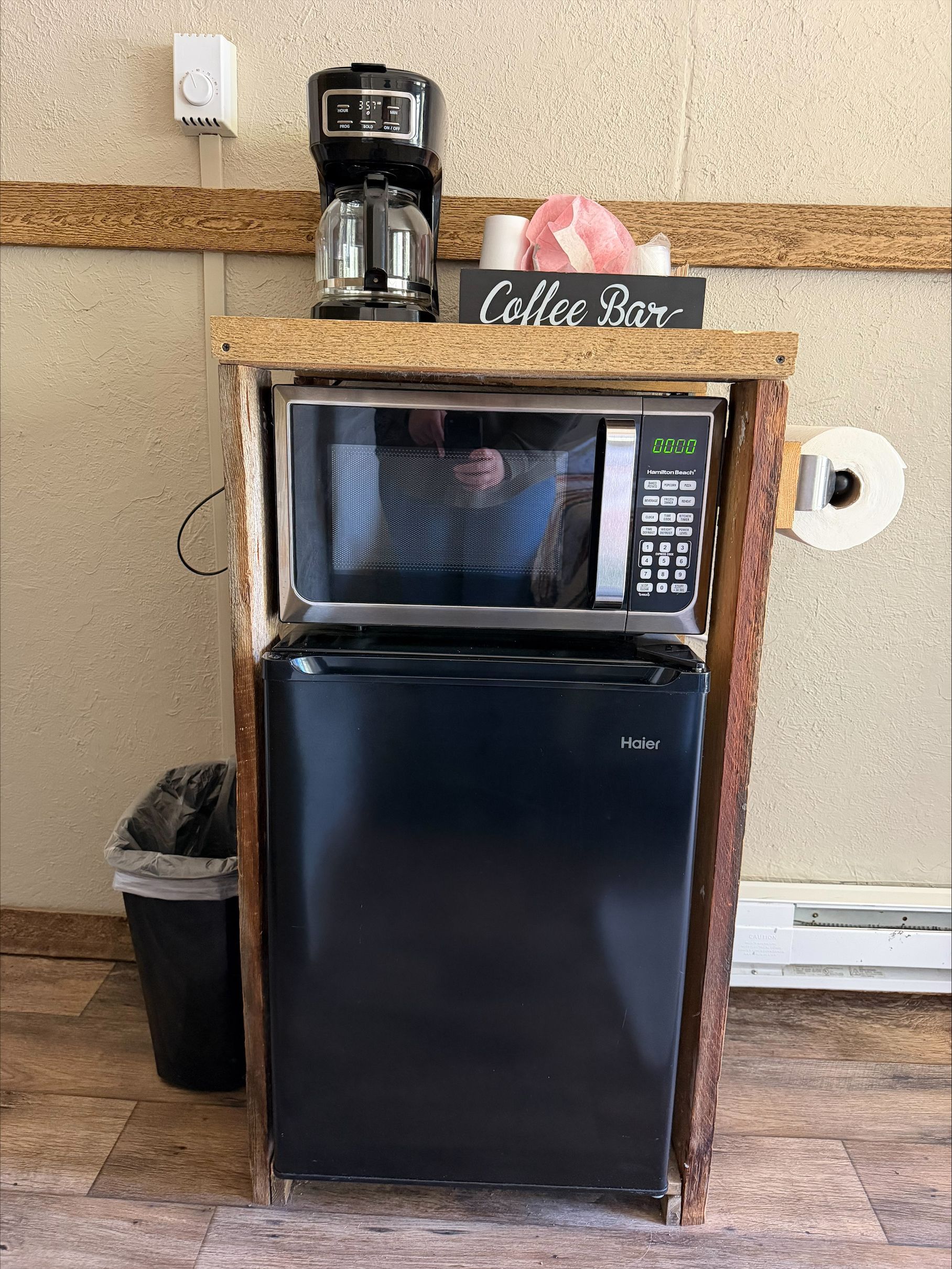 Compact coffee station with black microwave atop a mini fridge in a wood-trimmed nook